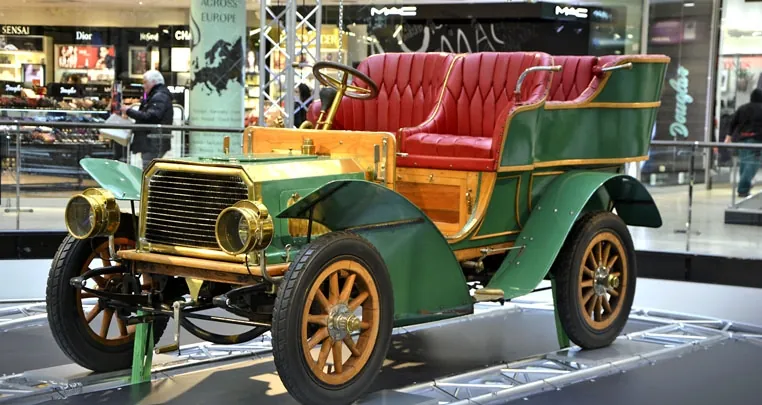 Benz Parsifal verde con asientos de cuero rojo y ruedas de madera, expuesto en un museo