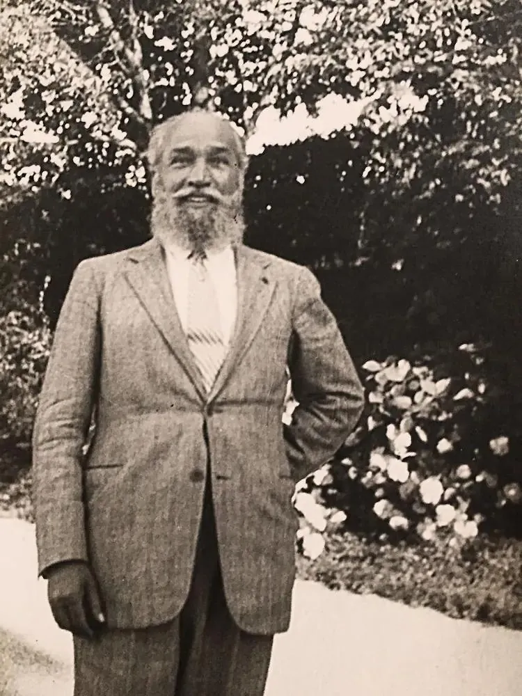 José Moroder standing in a garden, with a white beard and a light checked suit
