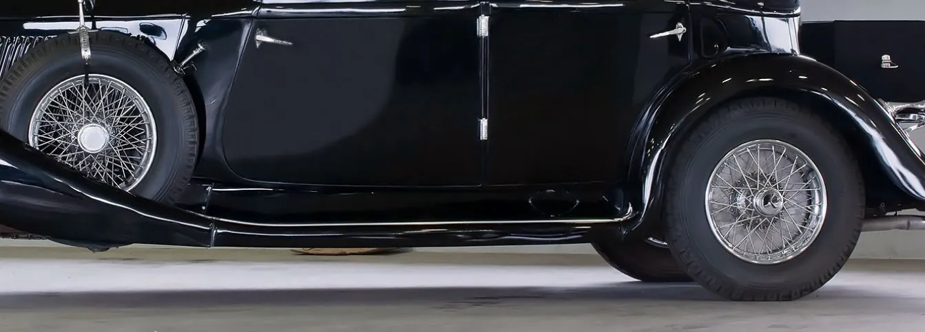 Side of a black classic car with a canvas hood and spoked wheel