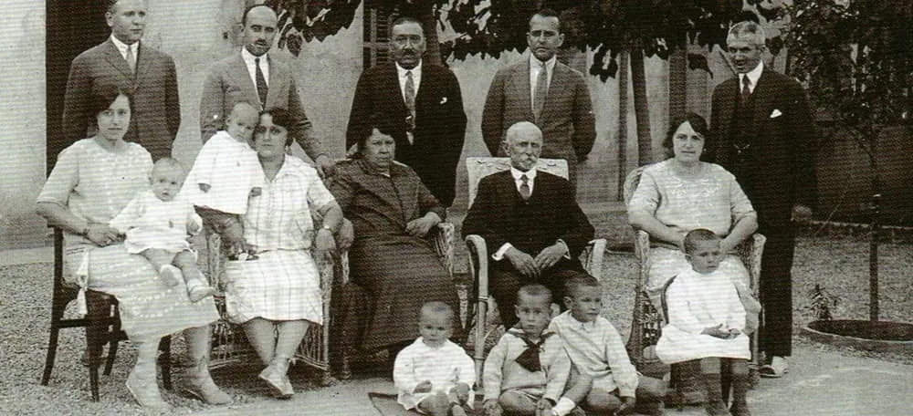 Portrait of the Brutau family, of Sucesores de B. Brutau, around 1920: sixteen people of three generations in a gravel garden with wicker armchairs, the white-bearded patriarch in the centre